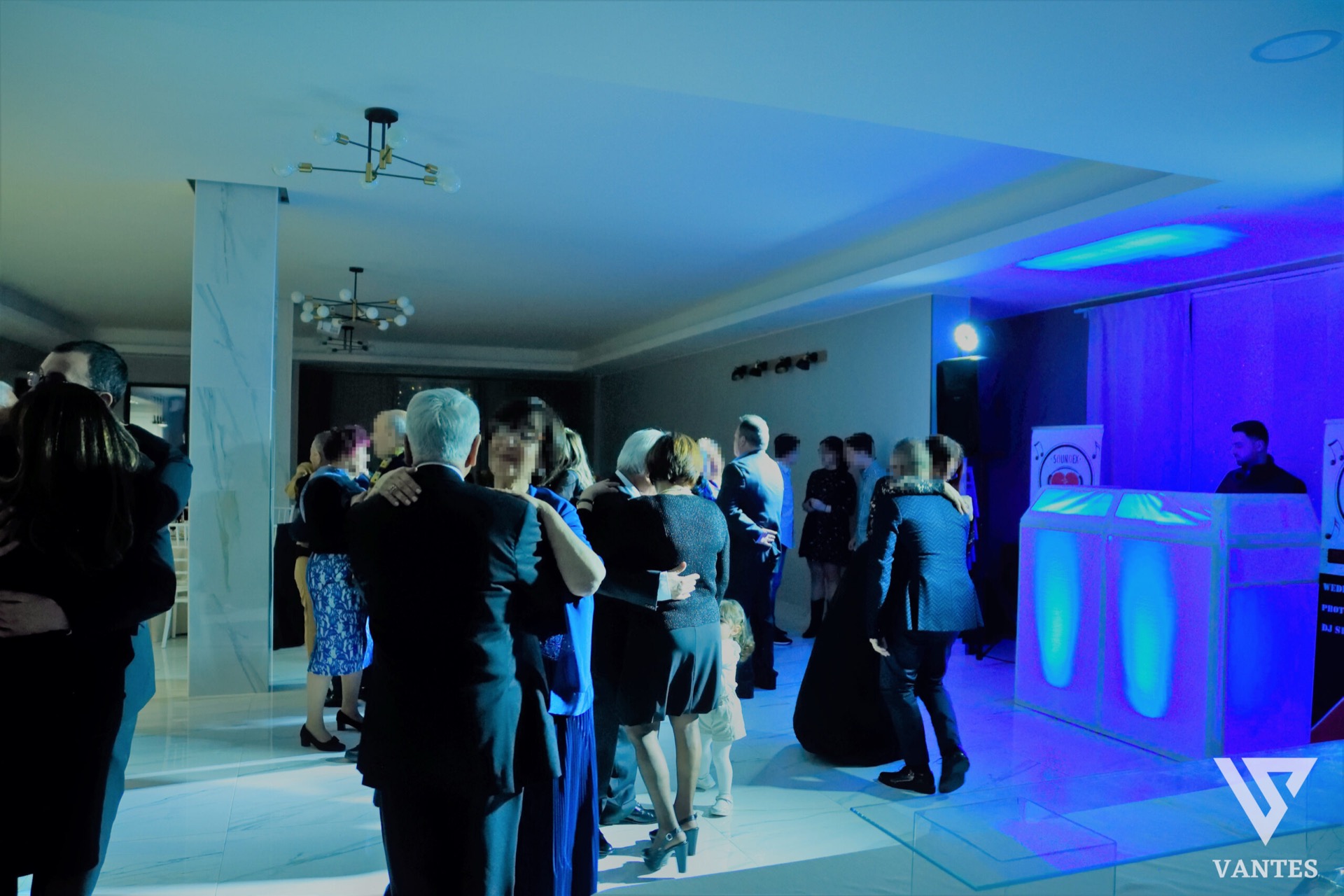 Sala con pista da ballo illuminata da luci blu e viola, ospiti che danzano in coppia e un DJ booth luminoso sulla destra. L'immagine mostra un momento vivace della festa, con colonne effetto marmo, pavimento lucido e atmosfera da serata danzante.