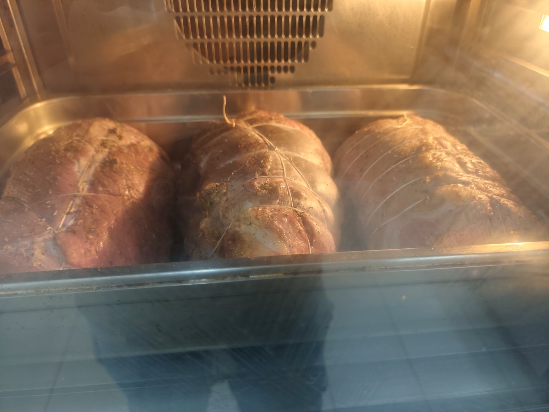 Tre arrosti legati cuociono in forno dentro una grande teglia metallica, ripresi attraverso il vetro dell'elettrodomestico. L'immagine documenta una fase di cottura della carne nelle preparazioni di Viglianisi Catering.