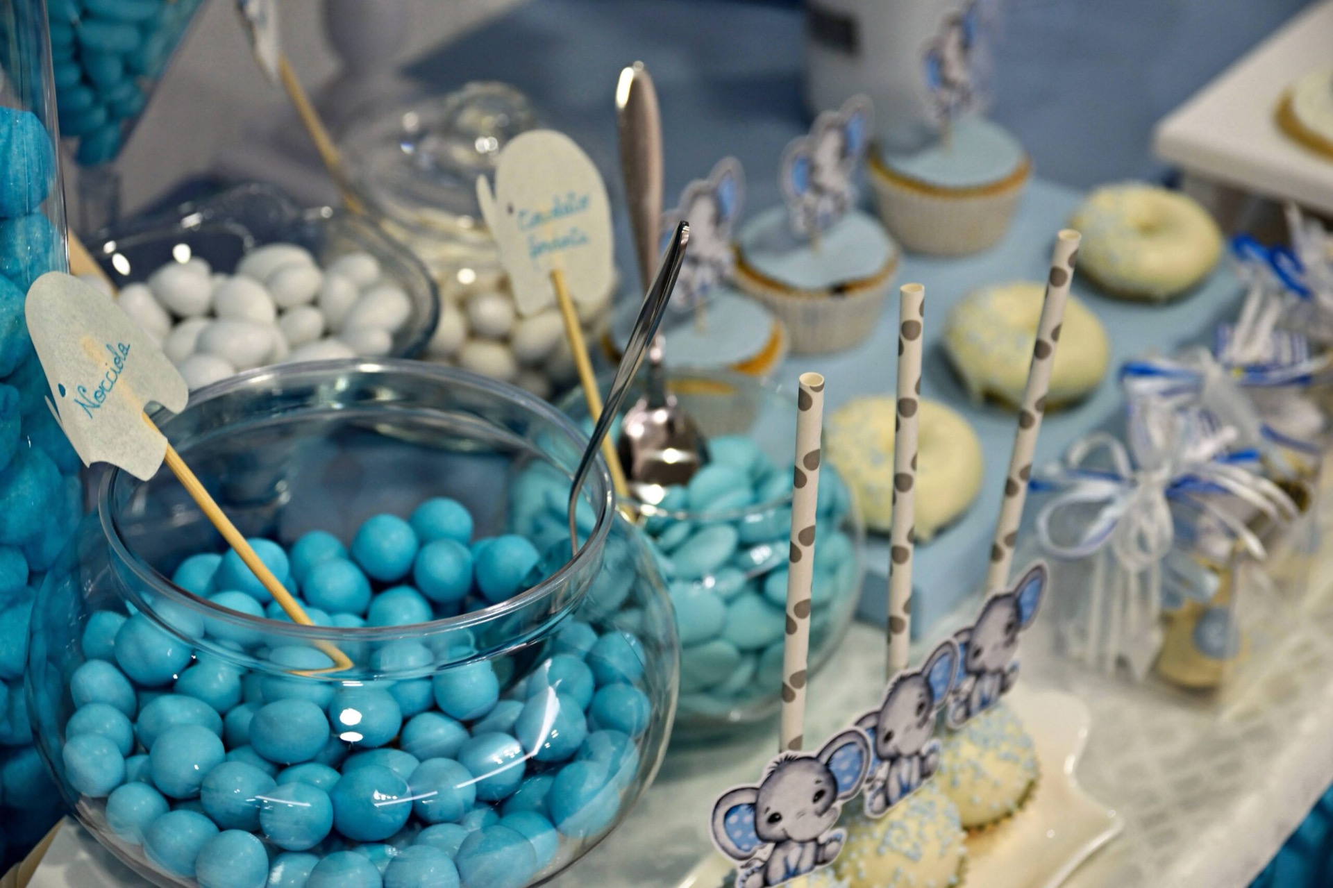 Confettata da battesimo allestita sui toni dell'azzurro con grandi contenitori di confetti, bicchieri decorativi e dolcetti monoporzione. Le decorazioni includono dettagli teneri e coordinati per un tema infantile elegante.