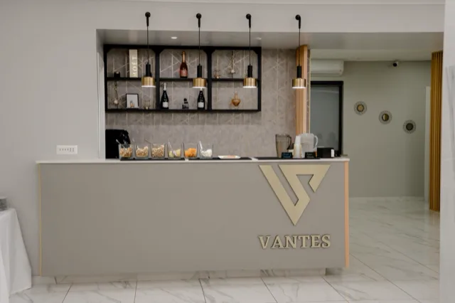 Banco bar interno della sala con linee minimal, bottiglie esposte su scaffalature retroilluminate e piccoli snack e bevande sul piano. L'ambiente è luminoso, ordinato e pensato per il servizio drink durante l'evento.
