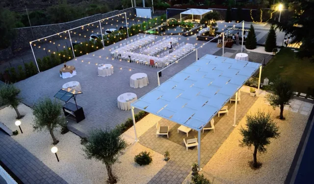 Vista dall'alto degli spazi esterni allestiti di sera, con lunghe tavolate bianche, tavoli rotondi d'appoggio, pergolato lounge e catenarie luminose sospese sull'area evento. L'immagine mostra con chiarezza la distribuzione ordinata delle varie zone del ricevimento.
