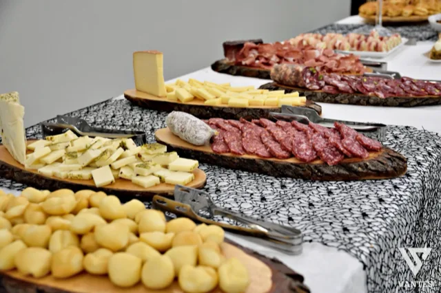 Buffet di salumi e formaggi allestito su taglieri rustici, con pinze da servizio, formaggi a cubetti, salami affettati e piccoli panini in primo piano. La composizione mette in evidenza la cura dell'angolo catering e la varietà della proposta salata.