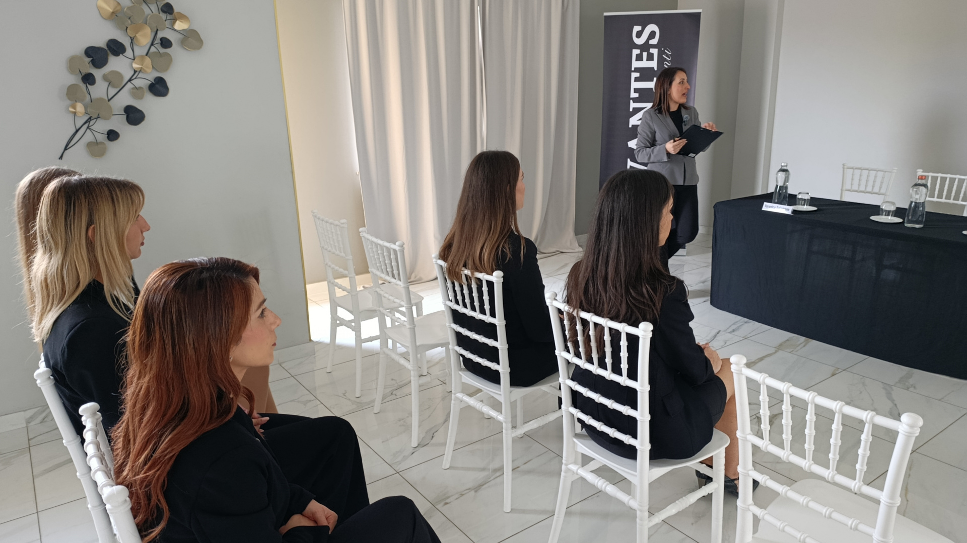Presentazione business in sala con relatrice in piedi accanto al banner Vantes e pubblico seduto davanti al tavolo relatori. L'immagine mostra un contesto raccolto e professionale per meeting o piccoli congressi.