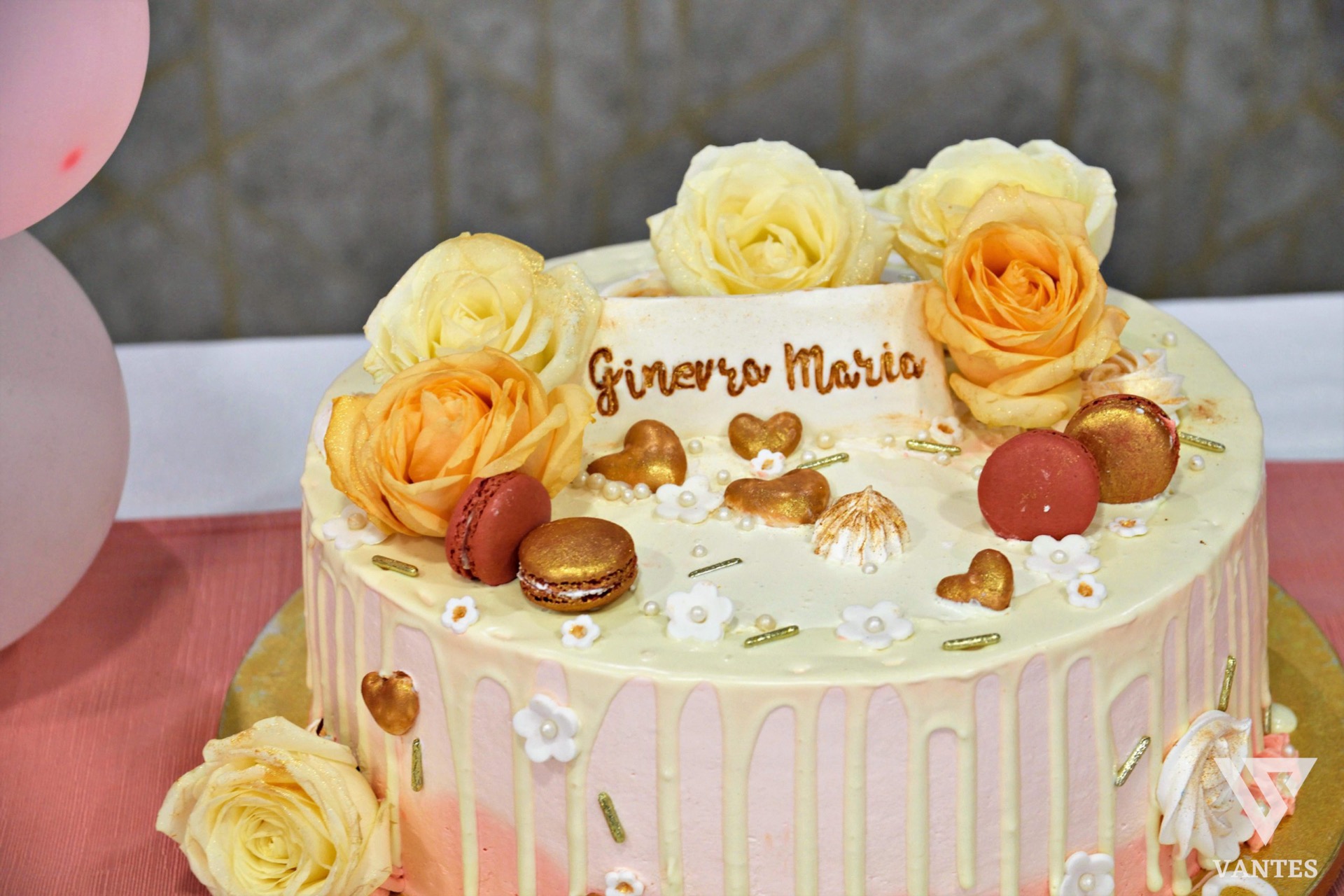 Torta da battesimo in sala, rosa e bianca, decorata con drip chiaro, rose fresche, macarons e piccoli dettagli dorati. La scritta con il nome Ginevra Maria personalizza l'allestimento della cerimonia.